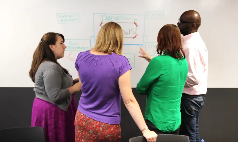 Team gathers at a whiteboard, using visual note taking to align on strategy and goals.