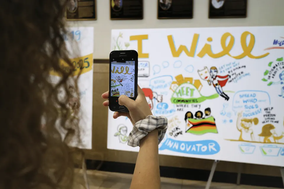 A participant photographing a social listening mural of student goals at an education conference