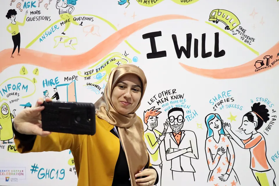 An attendee at the Grace Hopper Celebration taking a selfie with an ImageThink social listening mural